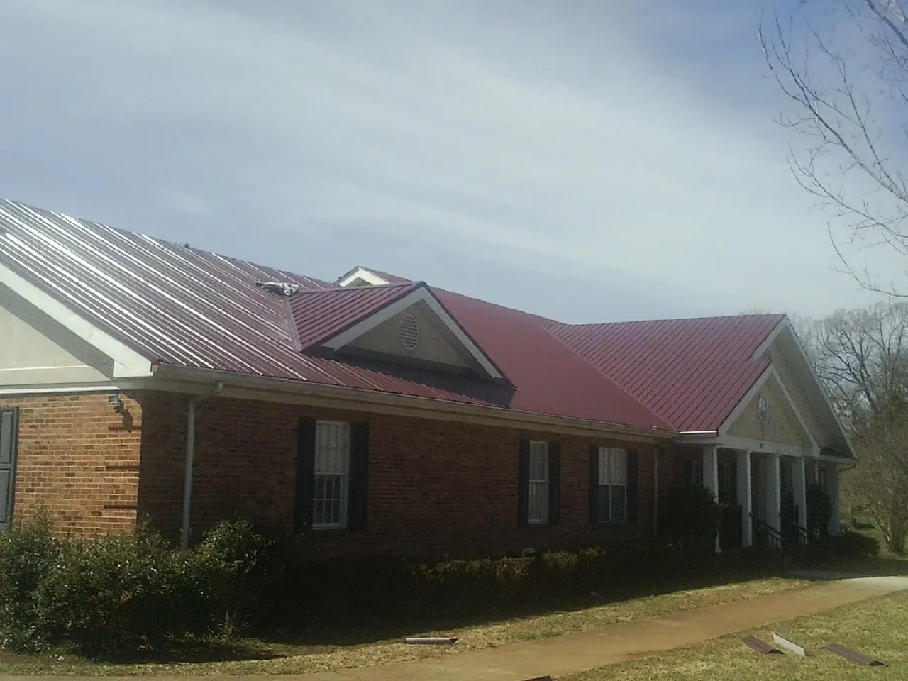 Red metal roof with gabled entries on a long brick building, from a Hail Damage Roof Repair job in Talbott