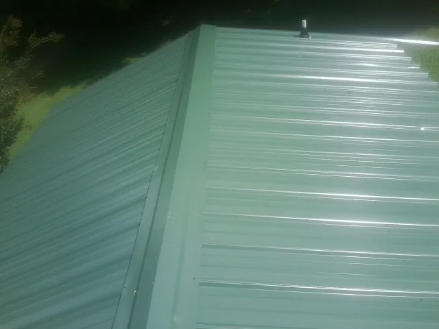 New green metal panels meeting at the ridge of a roof — Flat Roof Repair work by our crew in Talbott