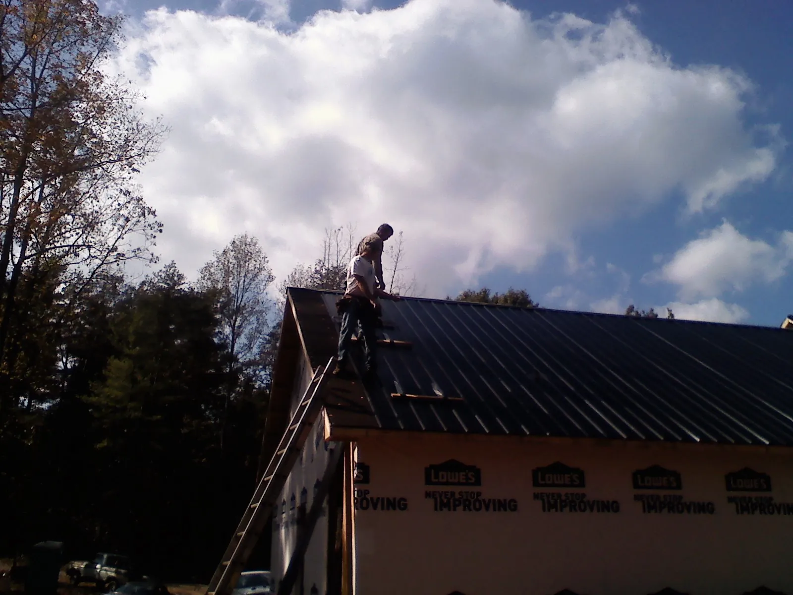 Roofer fastening dark metal panels high against a cloudy sky, from a Roof Inspection job in Talbott